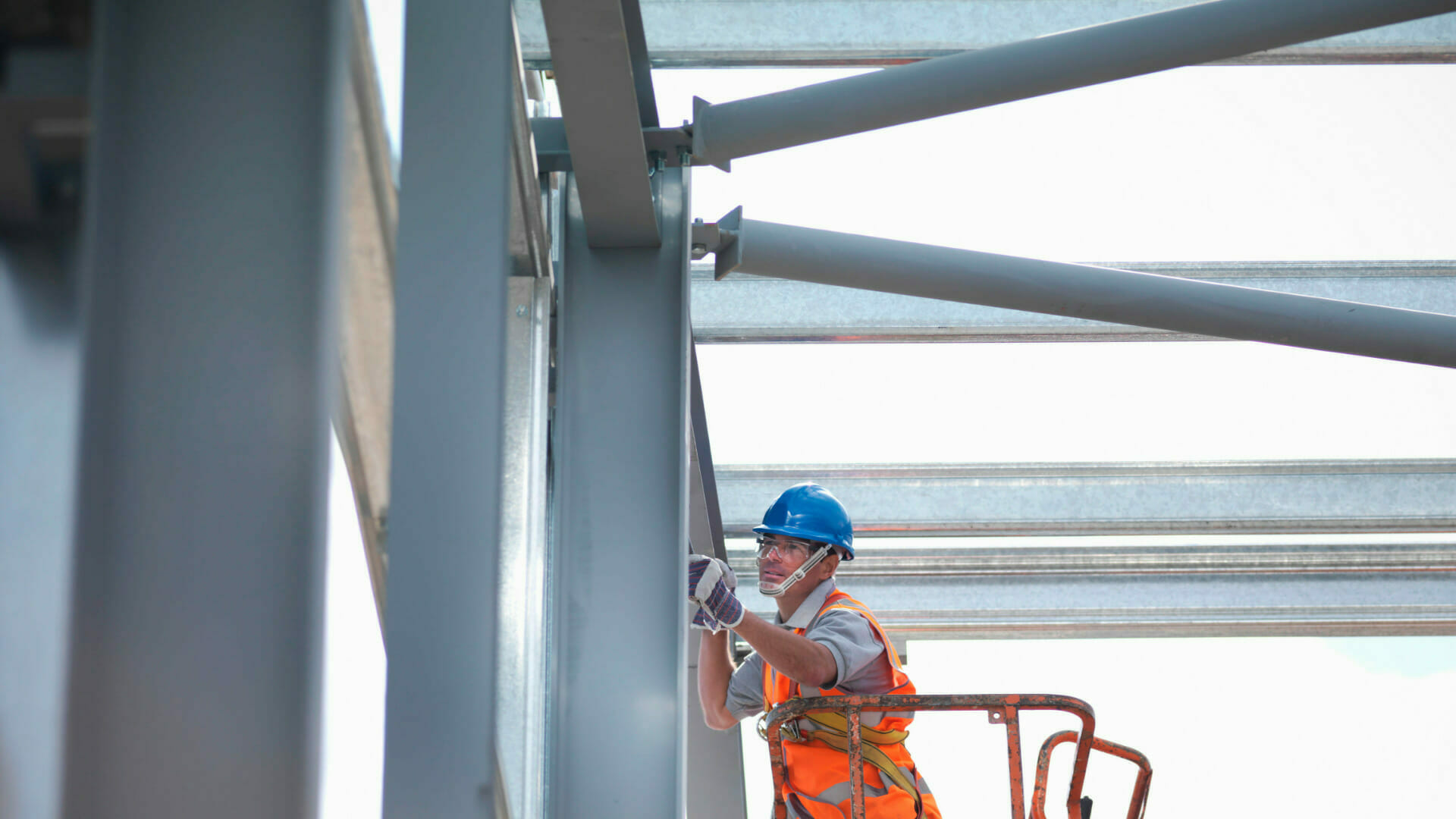 Man with hard hat, protective goggles, gloves and high-vis vest working up high on steel frame